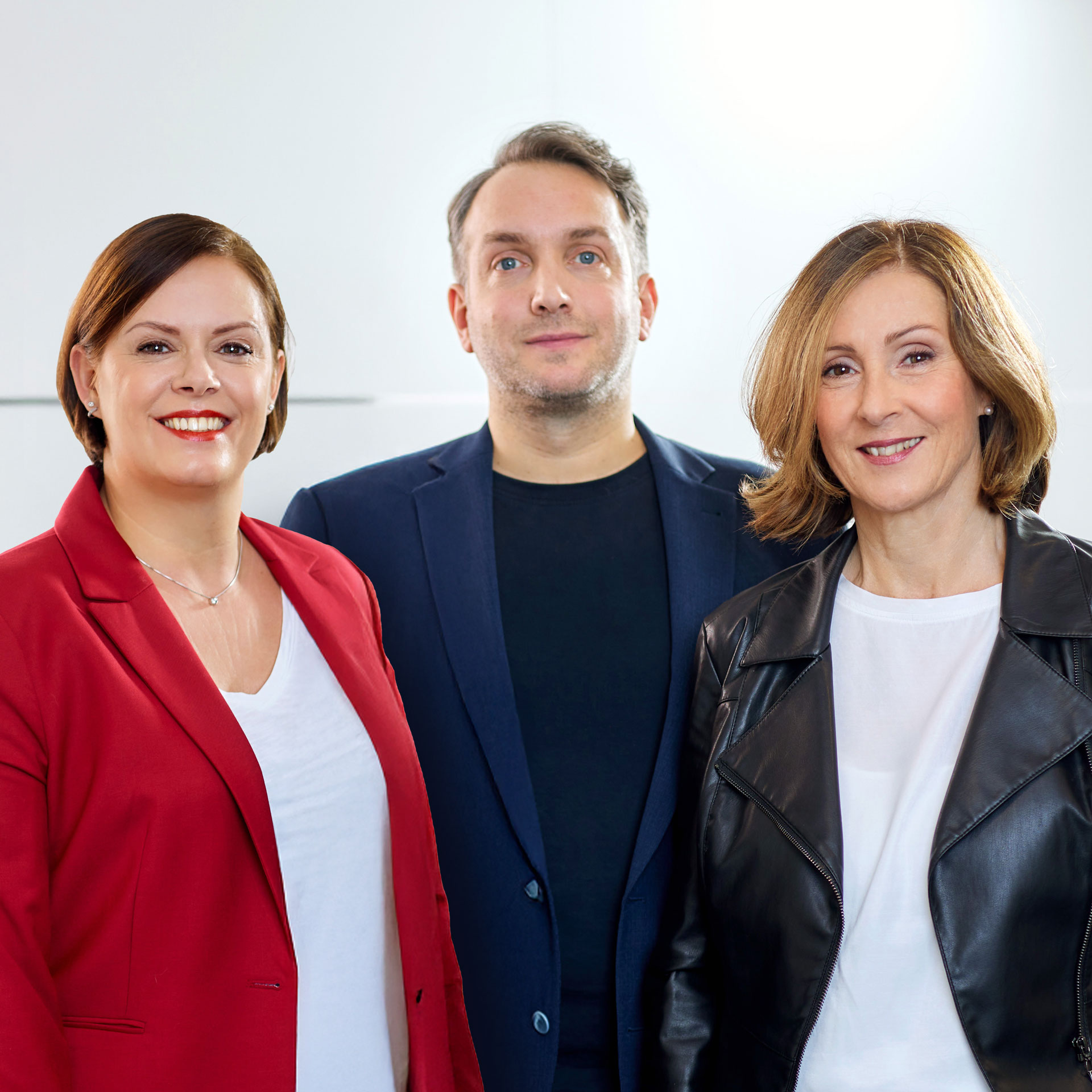 Drei Personen stehen vor einer Glasfront und lächeln.