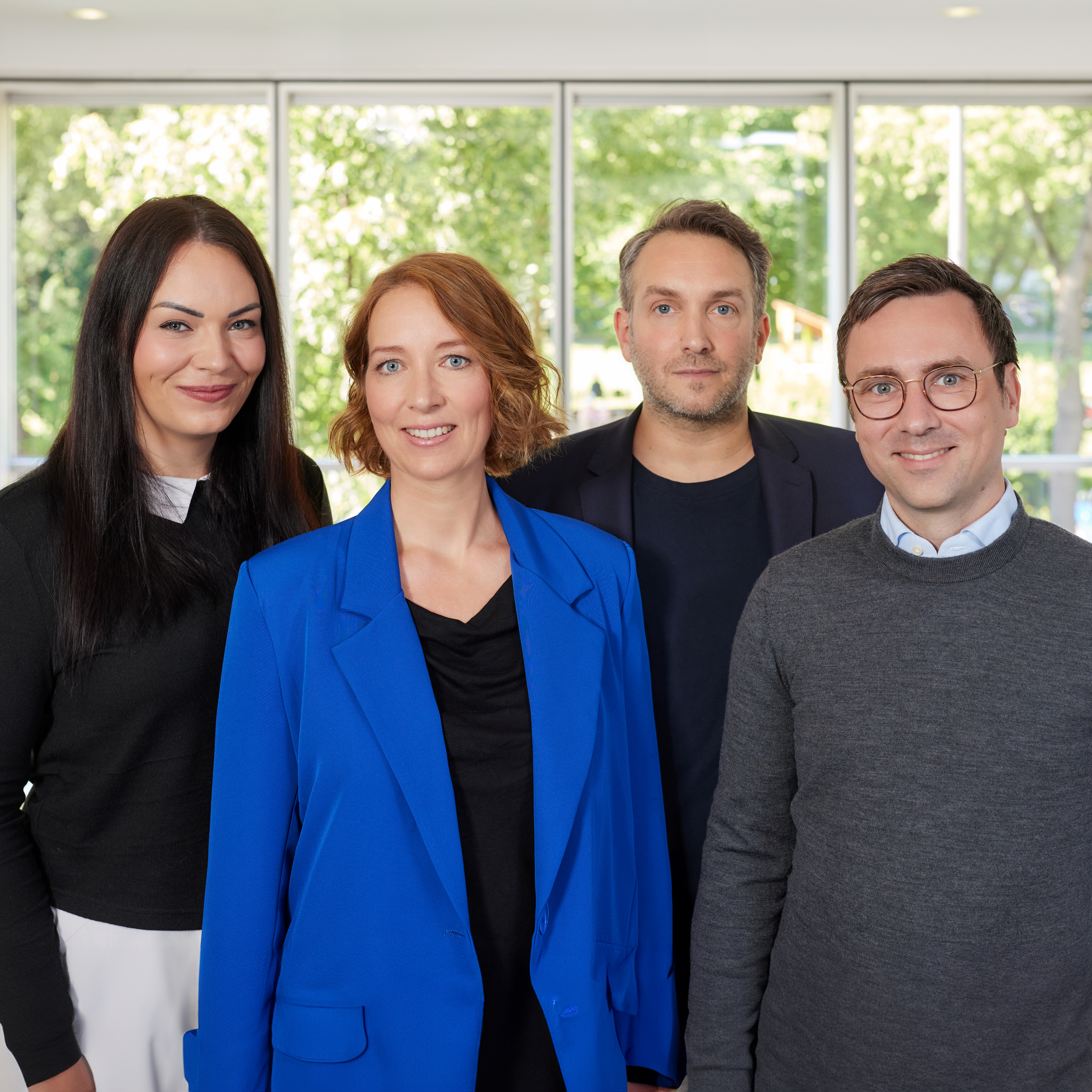 Vier Personen stehen vor einer Glasfront und lächeln.