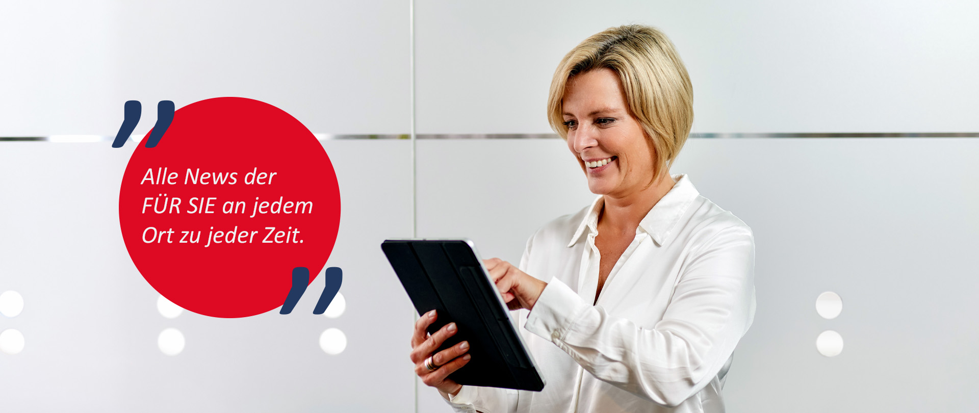 Eine Frau steht vor einer Glasscheibe mit einem IPad in der Hand und lächelt. 