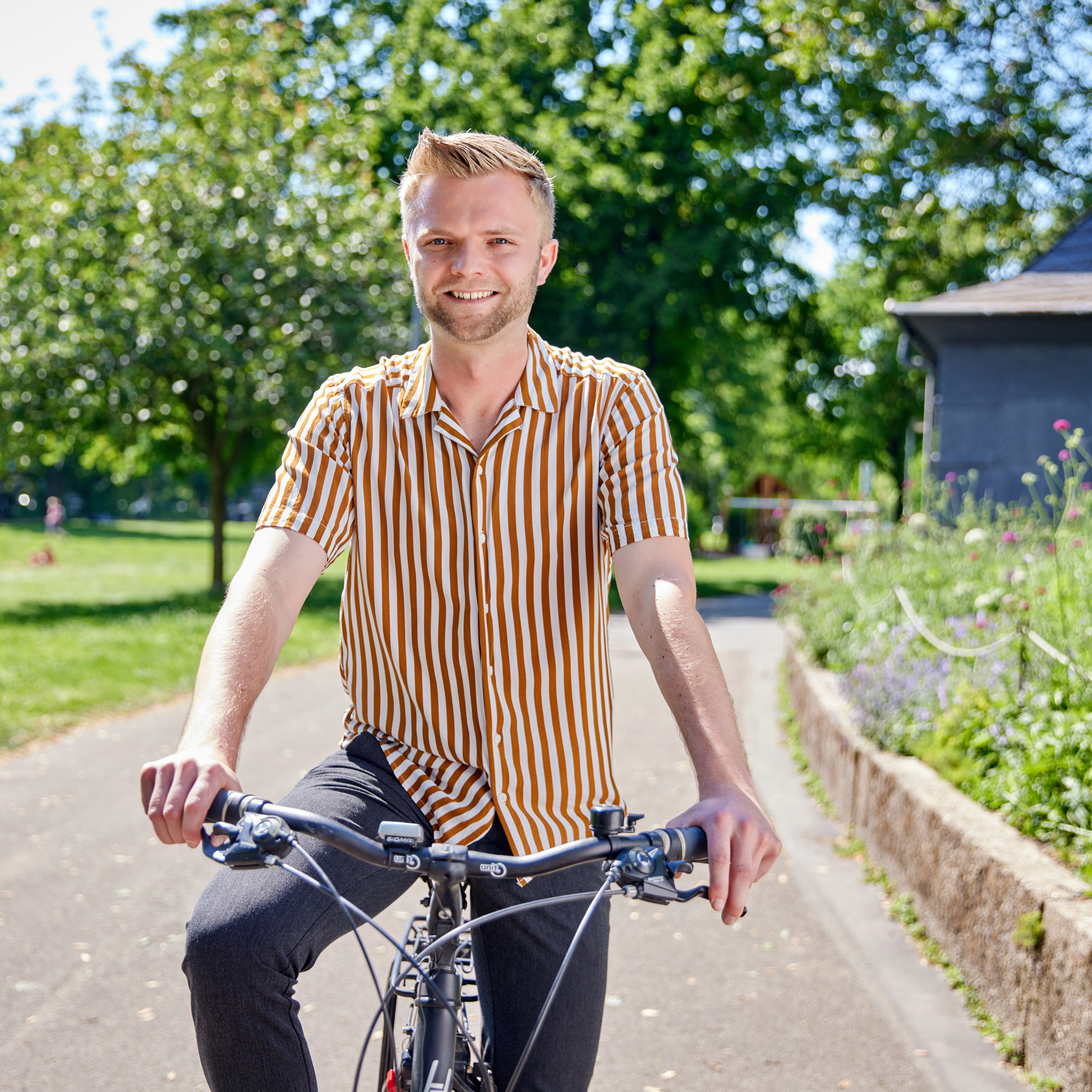Ein Mann sitzt auf einem Fahrrad in einem Park und lächelt.