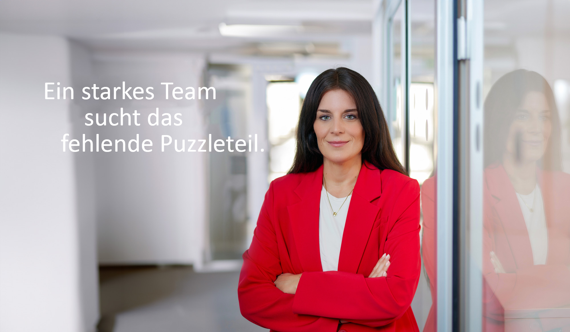 Eine Frau mit verschränkten Armen steht in einem Flur und lächelt.